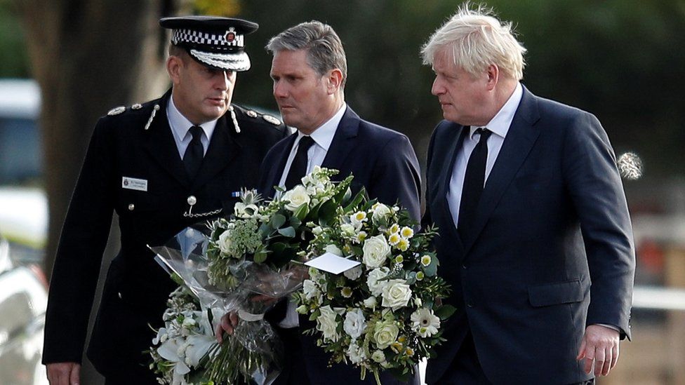Keir Starmer and Boris Johnson holding flowers at a funeral 